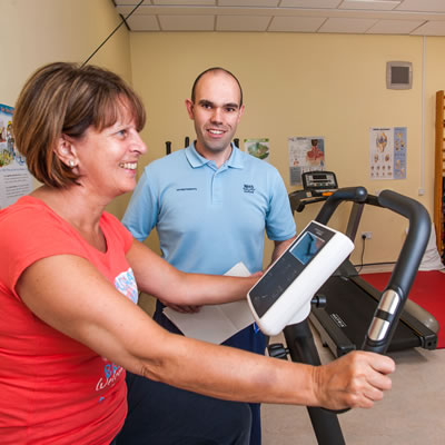 A male healthcare professional in the gym with a female patient who is riding a stationary bike