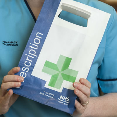 Close up of a healthcare professional or pharmacist with their face hidden holding an NHS prescription bag. 