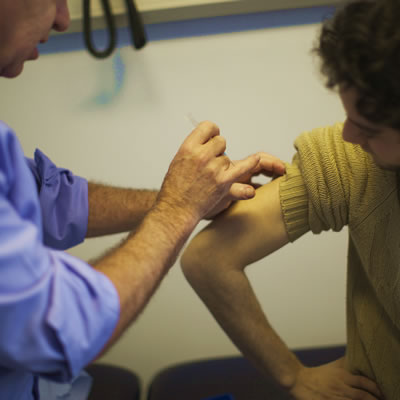 A doctor giving a young man a vaccination injection in the upper arm.