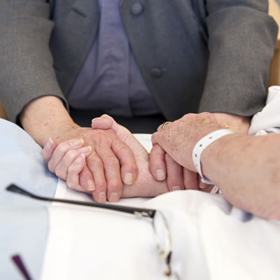 A female patient in a hospital bed holding hands with the hospital chaplain