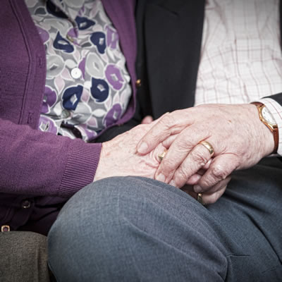 Close up photograph showing older couple holding hands