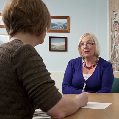 A mature woman patient consulting a GP in the surgery consulting room.