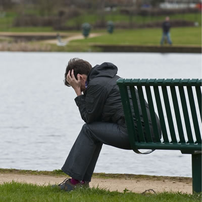 A person sitting on a park bench with her head in her hands. Expression of despair. Mental health and state of mind. 