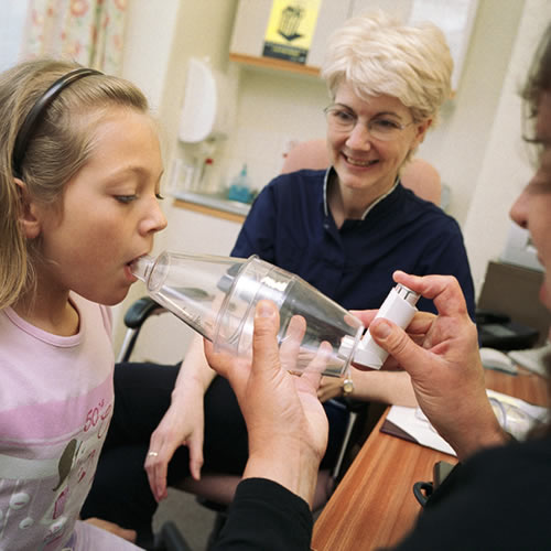 Child/ girl being shown how to use volumatic inhaler to treat asthma. Mother and nurse.